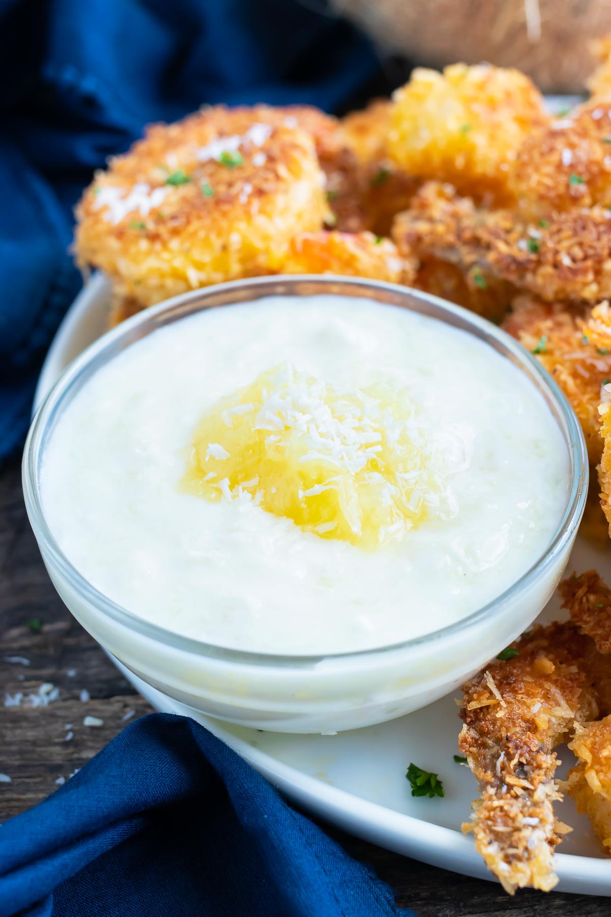 A white yogurt sauce with some crushed pineapple on top with a platter of coconut shrimp.