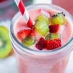 A strawberry kiwi smoothie is served with fresh fruit on top and a straw.
