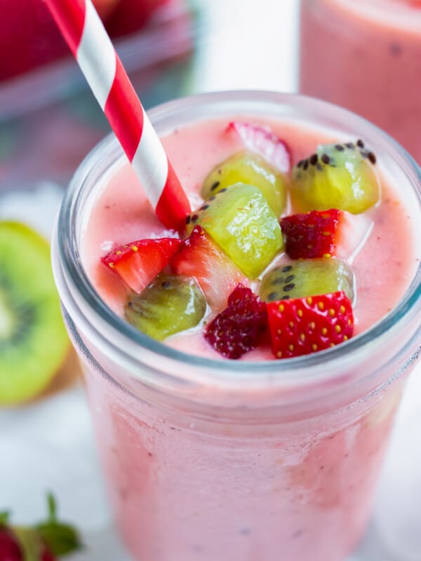 A strawberry kiwi smoothie is served with fresh fruit on top and a straw.