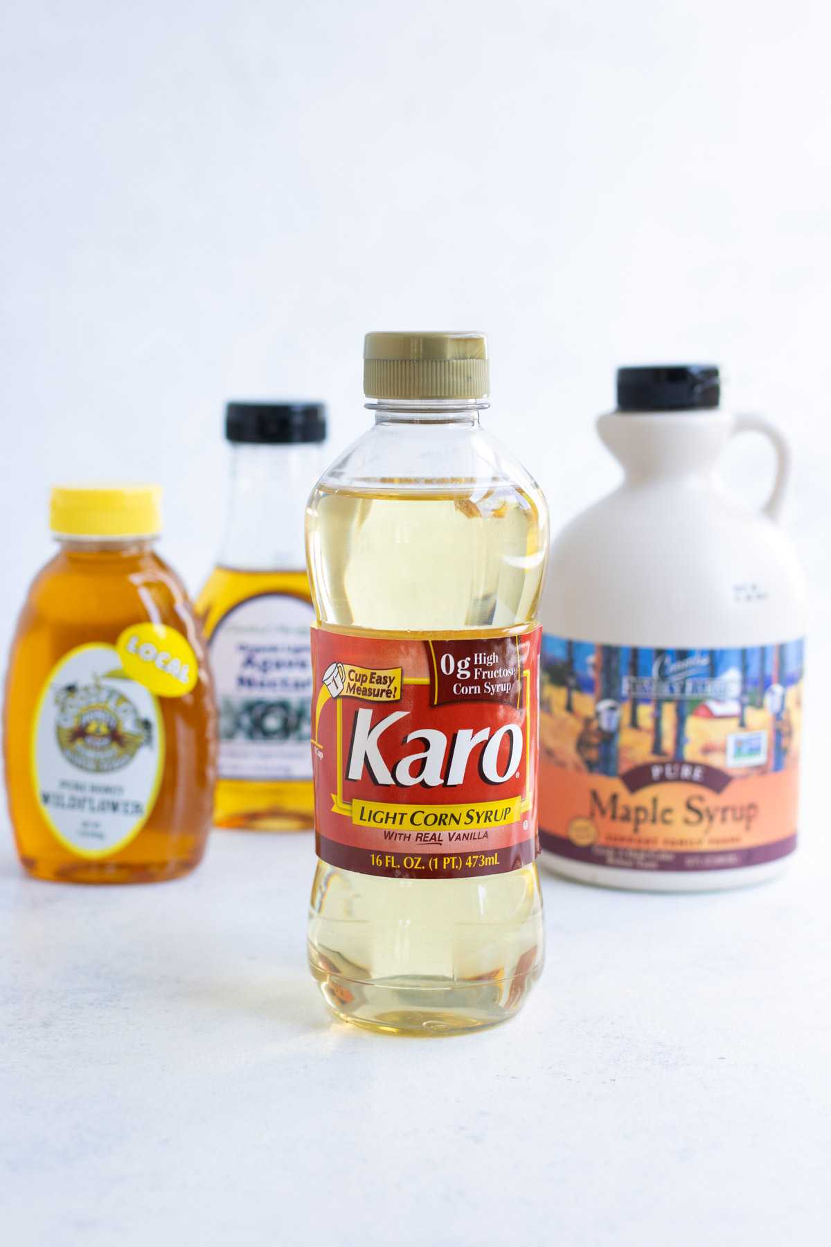 Maple syrup, honey, corn syrup, and agave nectar lined up on a countertop.
