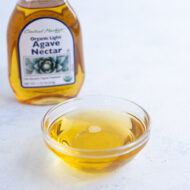 Agave nectar in a glass bowl on the countertop with the original container in the background.