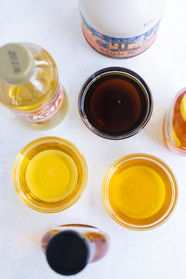 Top view of maple syrup, agave nectar, and honey poured in clear glass bowls.