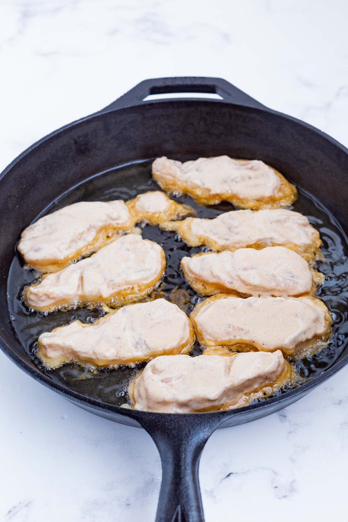 Beer battered fish is cooked in a skillet.