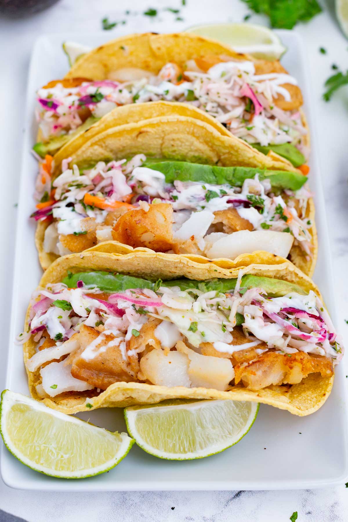 Three Baja fish tacos are served with fresh lime wedges.