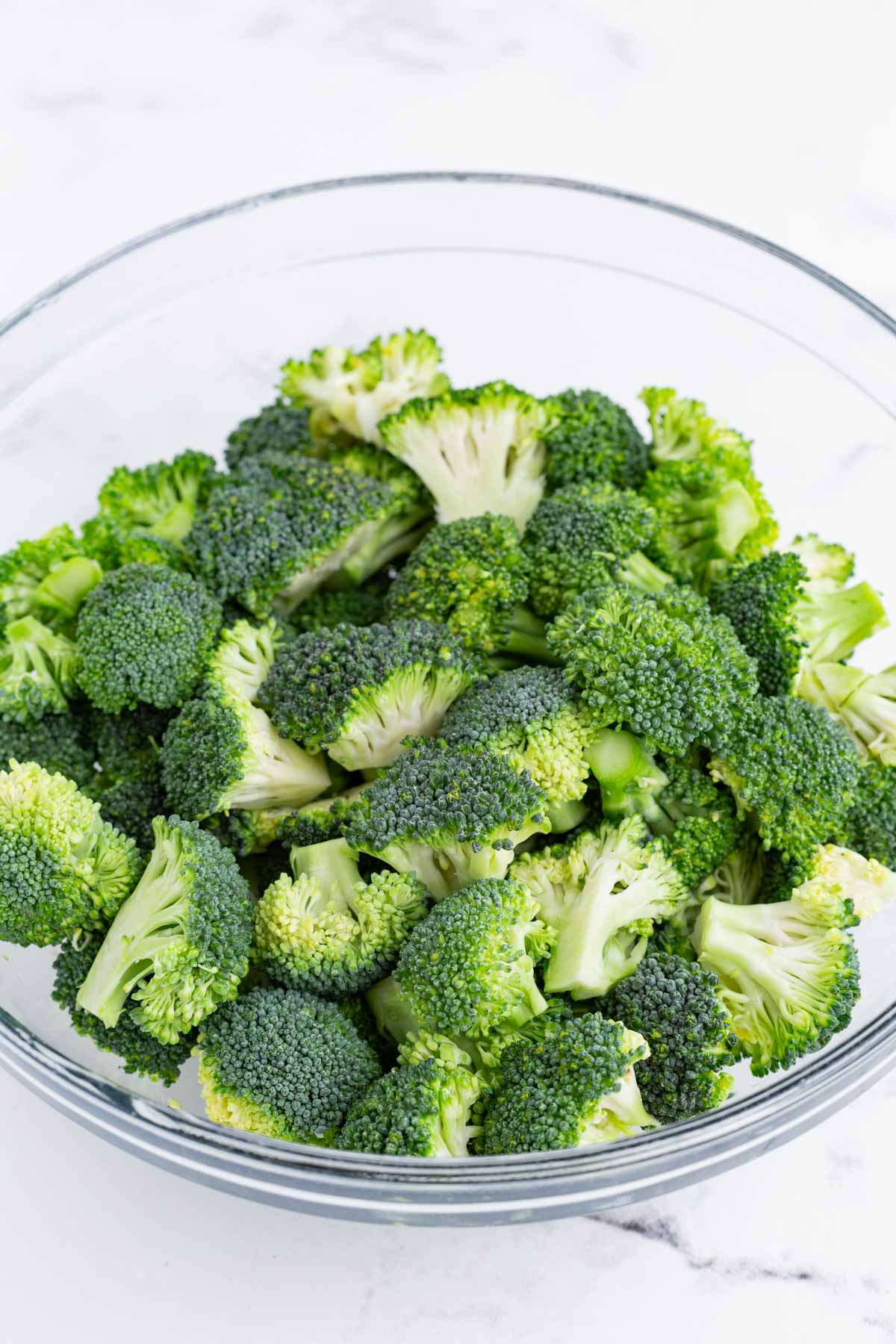 Cut up broccoli is added to a glass bowl.