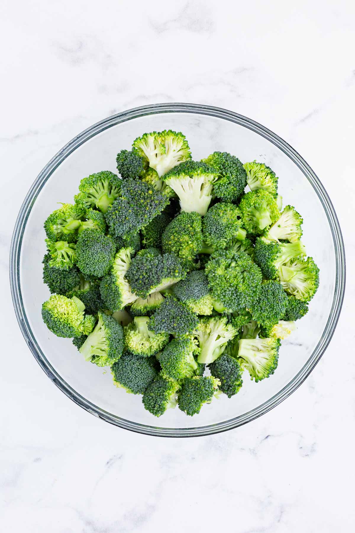 Cut up broccoli is added to a glass bowl.