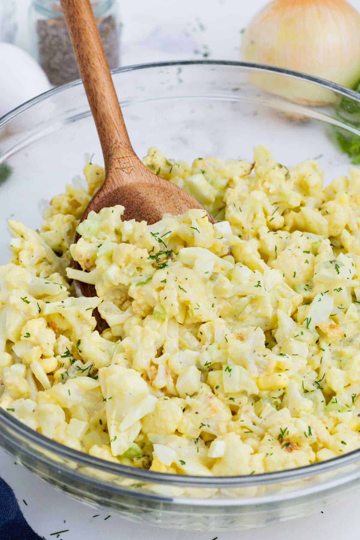 A wooden spoon is used to serve cauliflower potato salad.