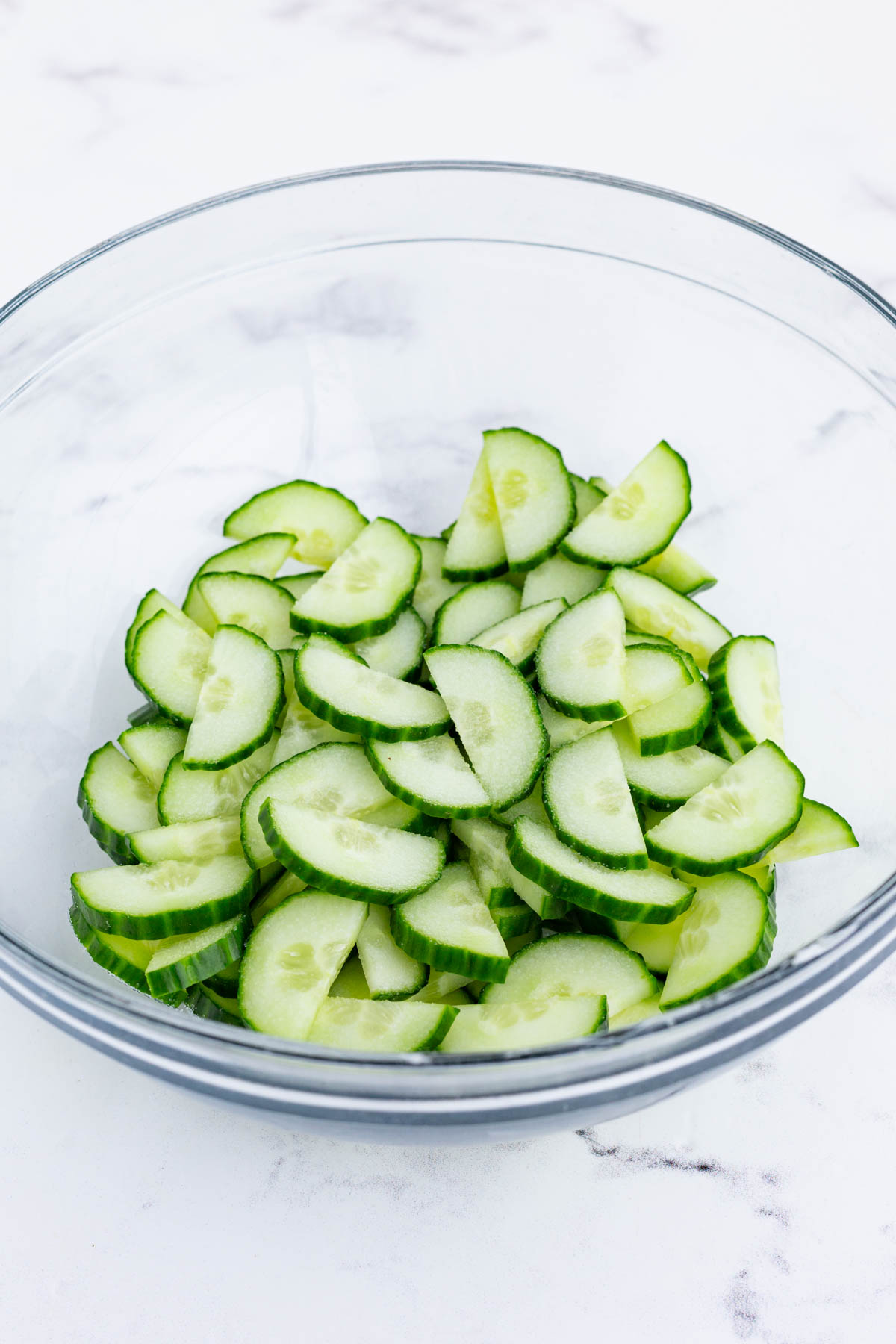 Salt is drizzled on sliced cucumbers in a bowl.