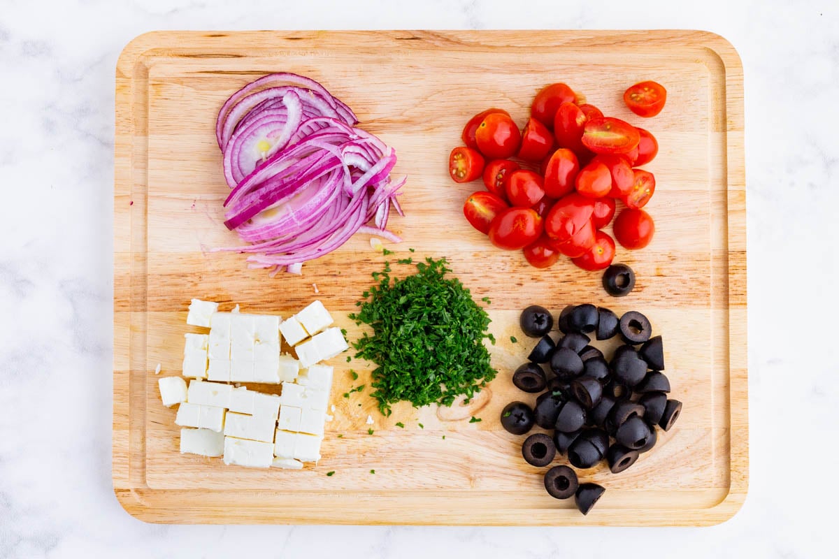 Onions, tomatoes, olives, feta, and parsley are chopped.