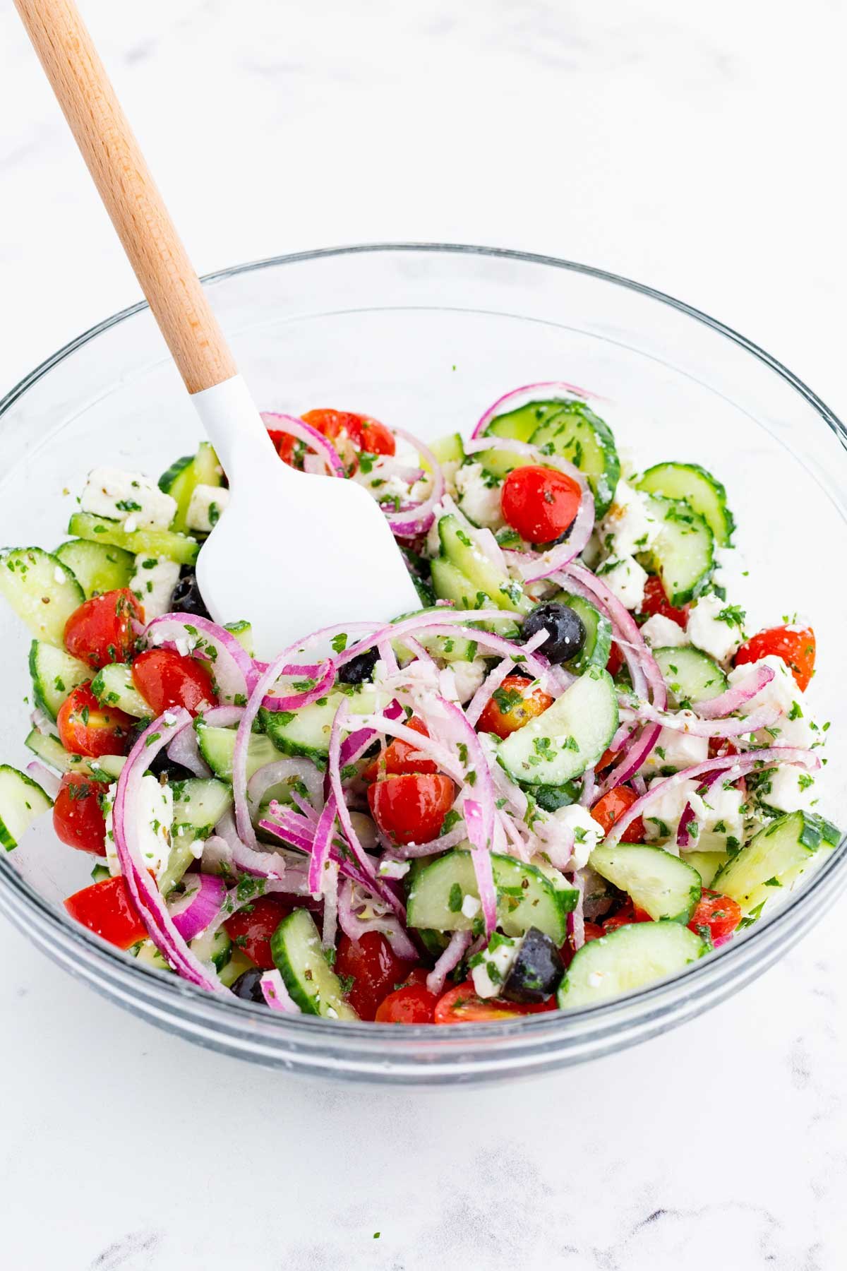 The Greek salad is stirred with a spatula.