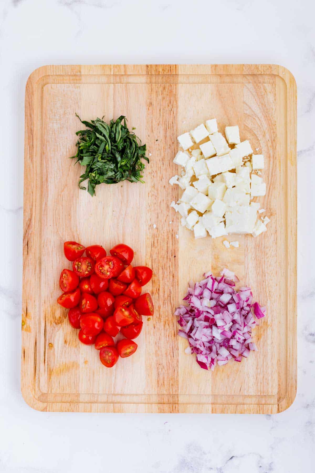 Basil, onion, tomatoes, and feta cheese are cut up.