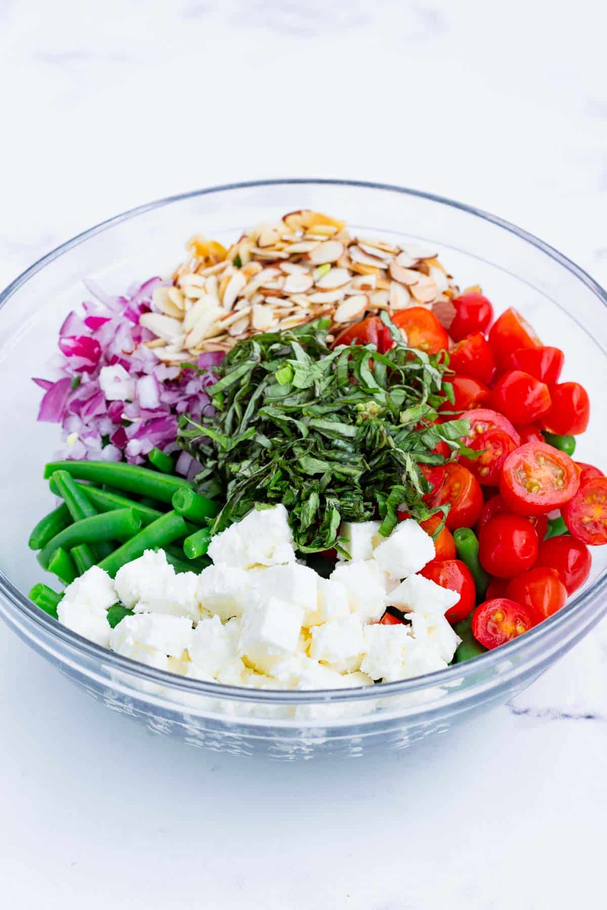 Green bean salad ingredients are combined in a glass bowl.