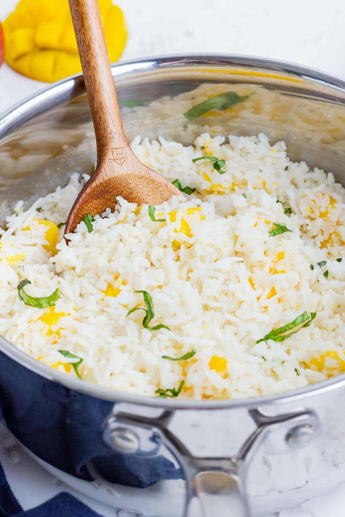A wooden spoon stirs mango into coconut rice.