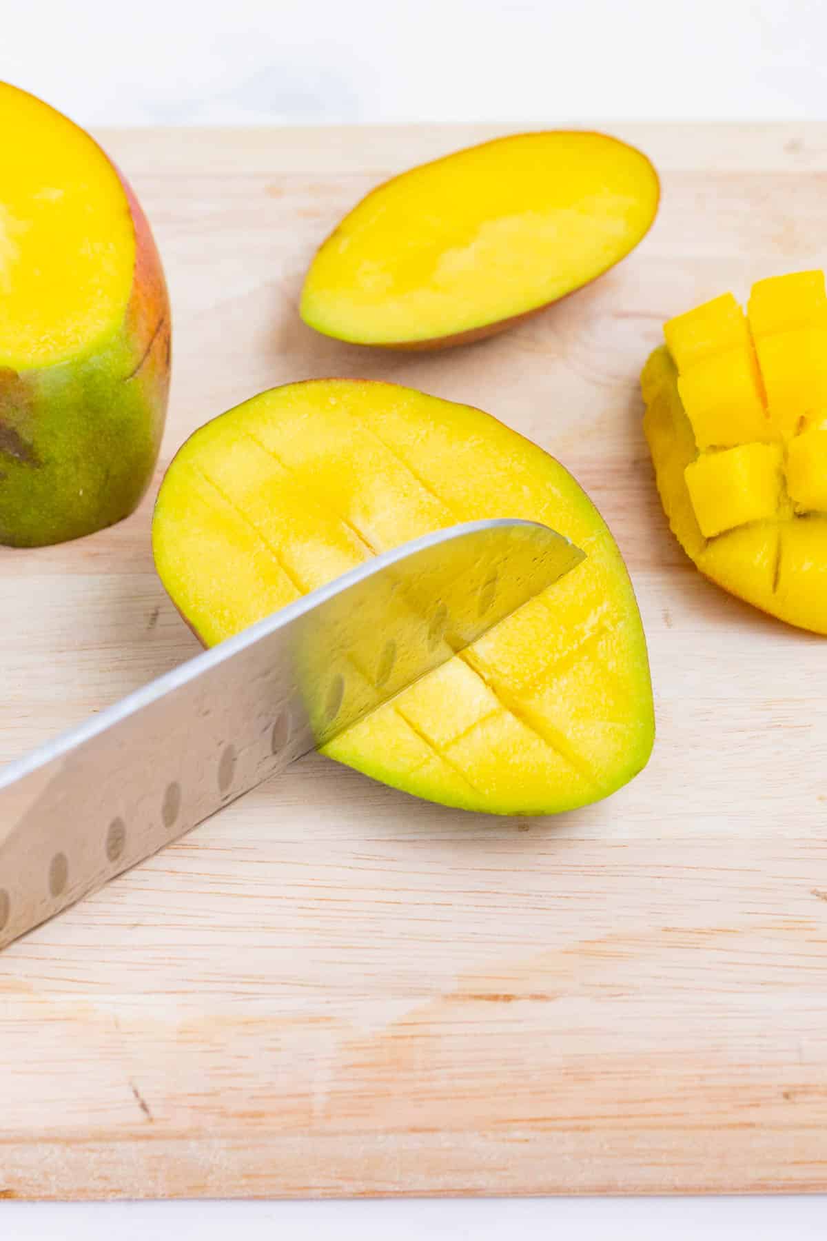 A sharp knife cuts a mango into small pieces.