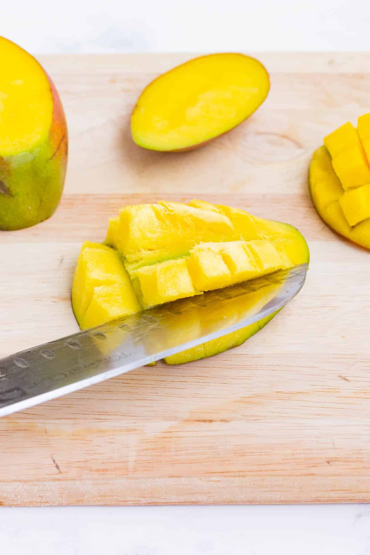 A sharp knife cuts a mango into small pieces.
