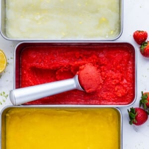 An ice cream scoop is scooping up some homemade sorbet recipe from a metal tin.