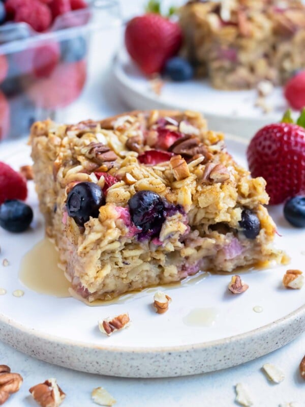 The baked oatmeal is served on a plate with fresh berries and syrup.