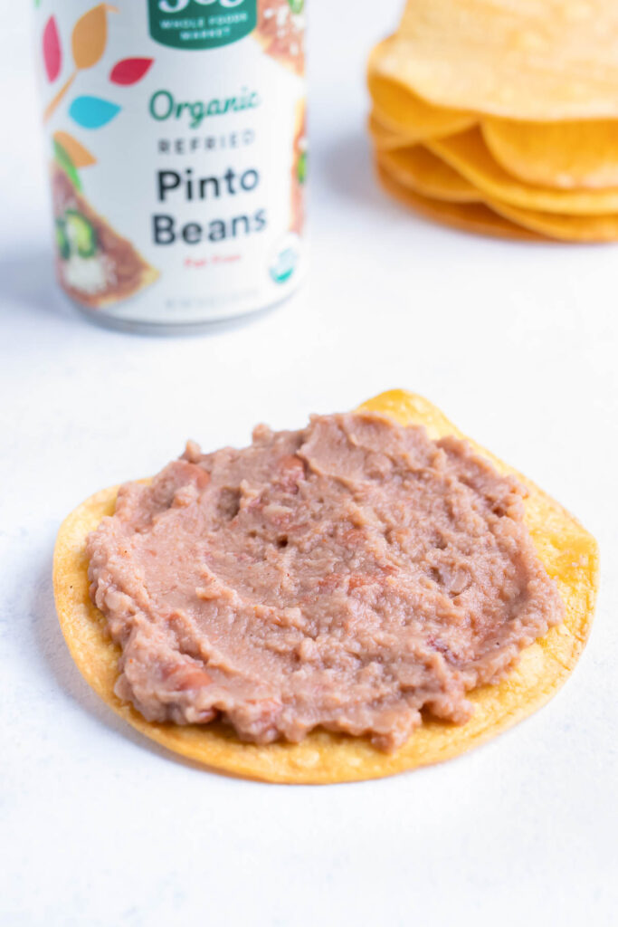 Refried beans are spread on a tostada shell.
