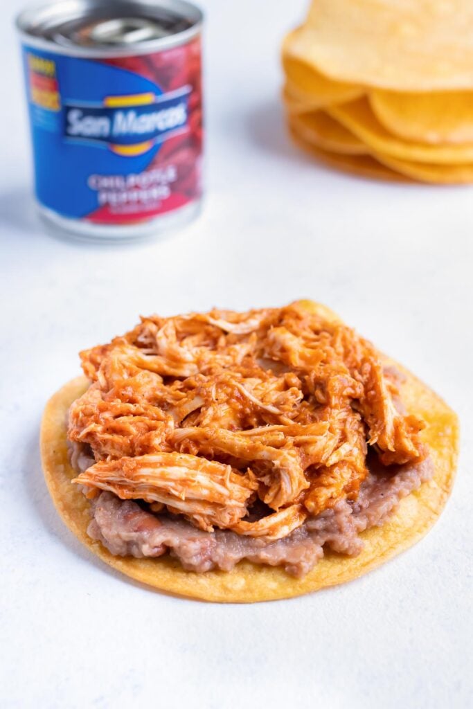 Refried beans and chicken are spread over the baked corn tortillas.