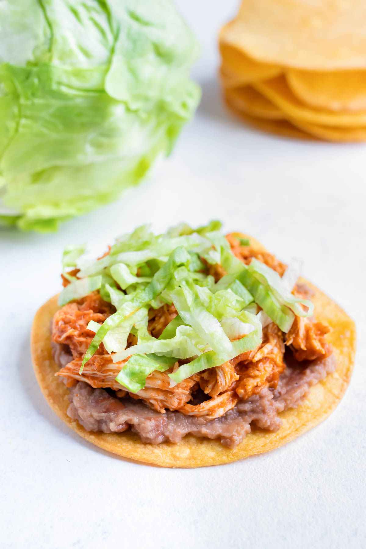 Lettuce is layered on to the chicken tinga tostada.