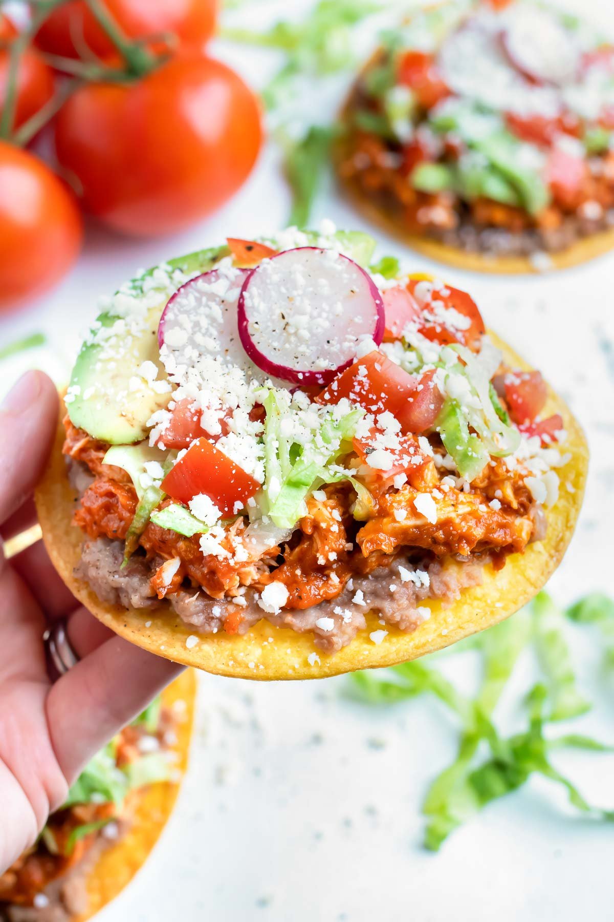 A chicken tinga tostada is held in a hand for an appetizer.