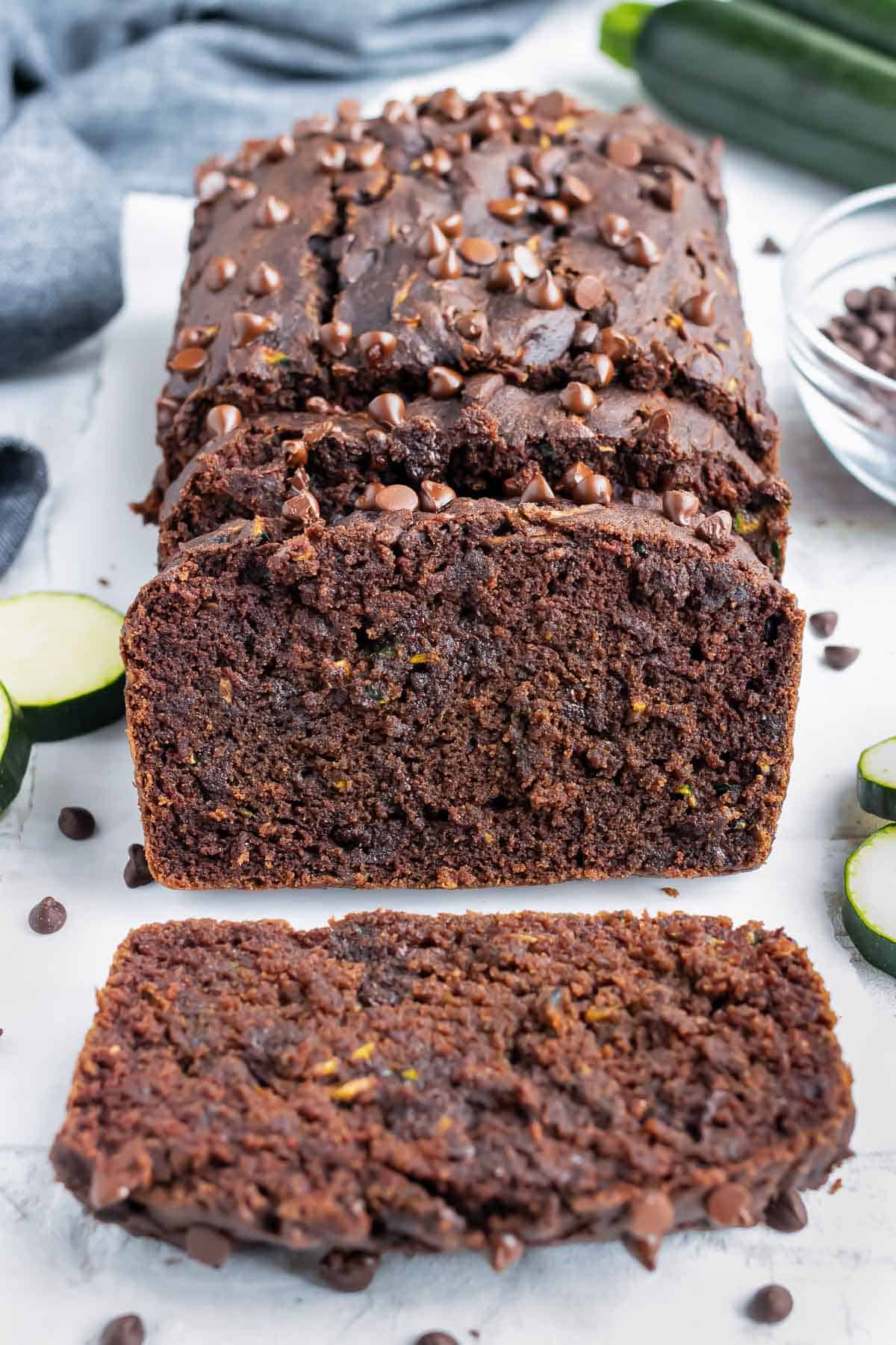 A slice of zucchini bread with chocolate chips on a table next to a grey napkin.