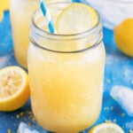 Homemade frozen lemonade in a glass mason jar with a blue straw next to a lemon wedge.