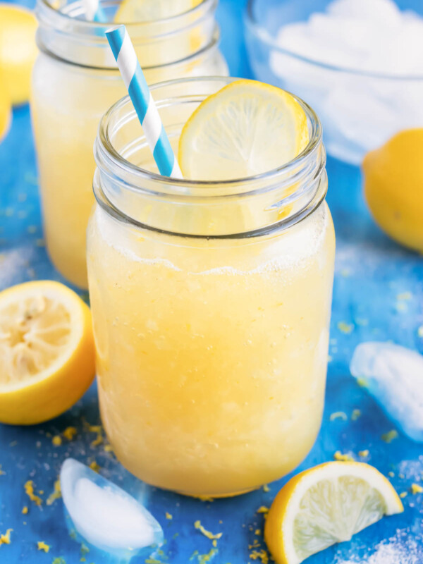 Homemade frozen lemonade in a glass mason jar with a blue straw next to a lemon wedge.
