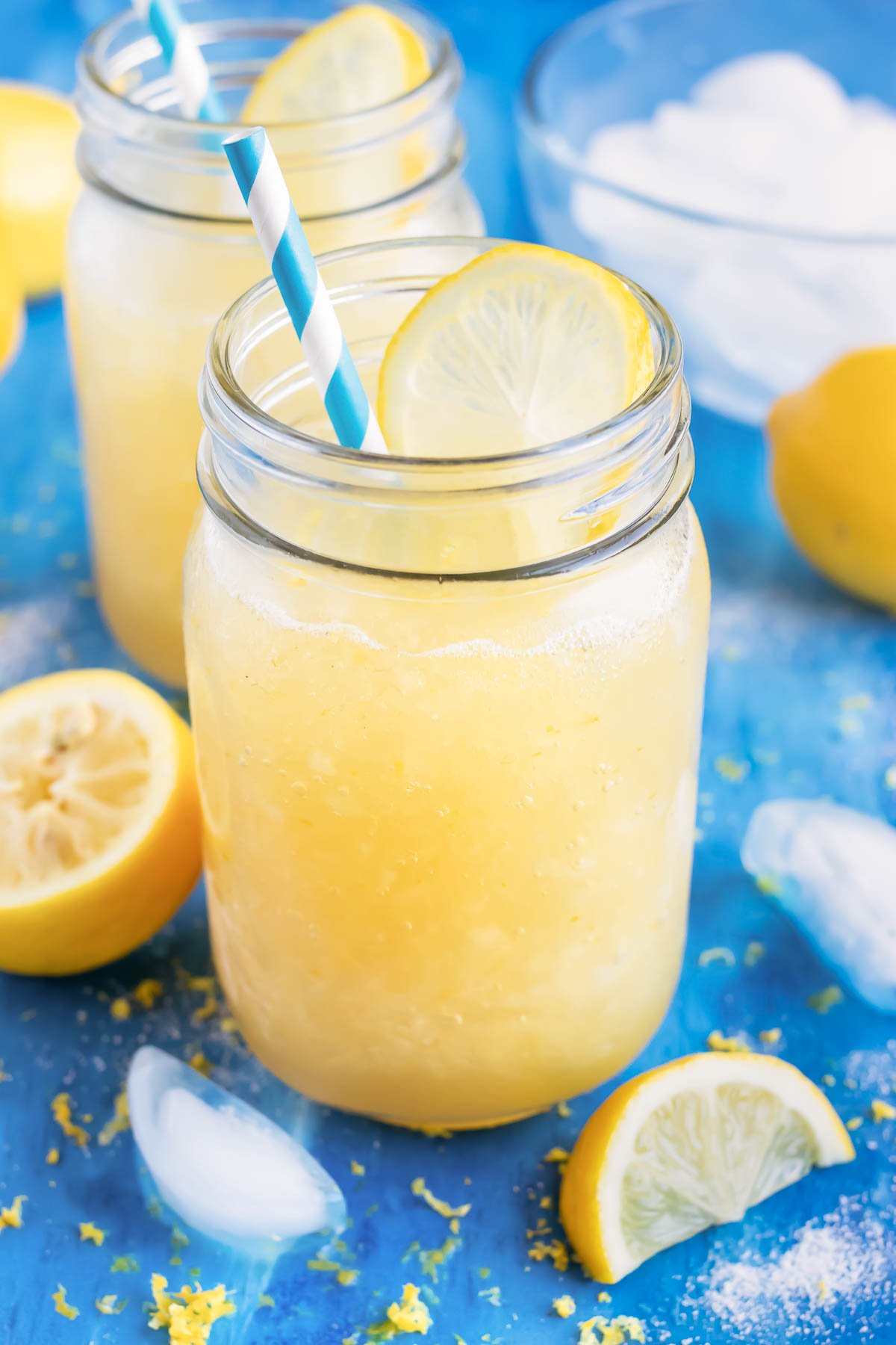 Homemade frozen lemonade in a glass mason jar with a blue straw next to a lemon wedge.