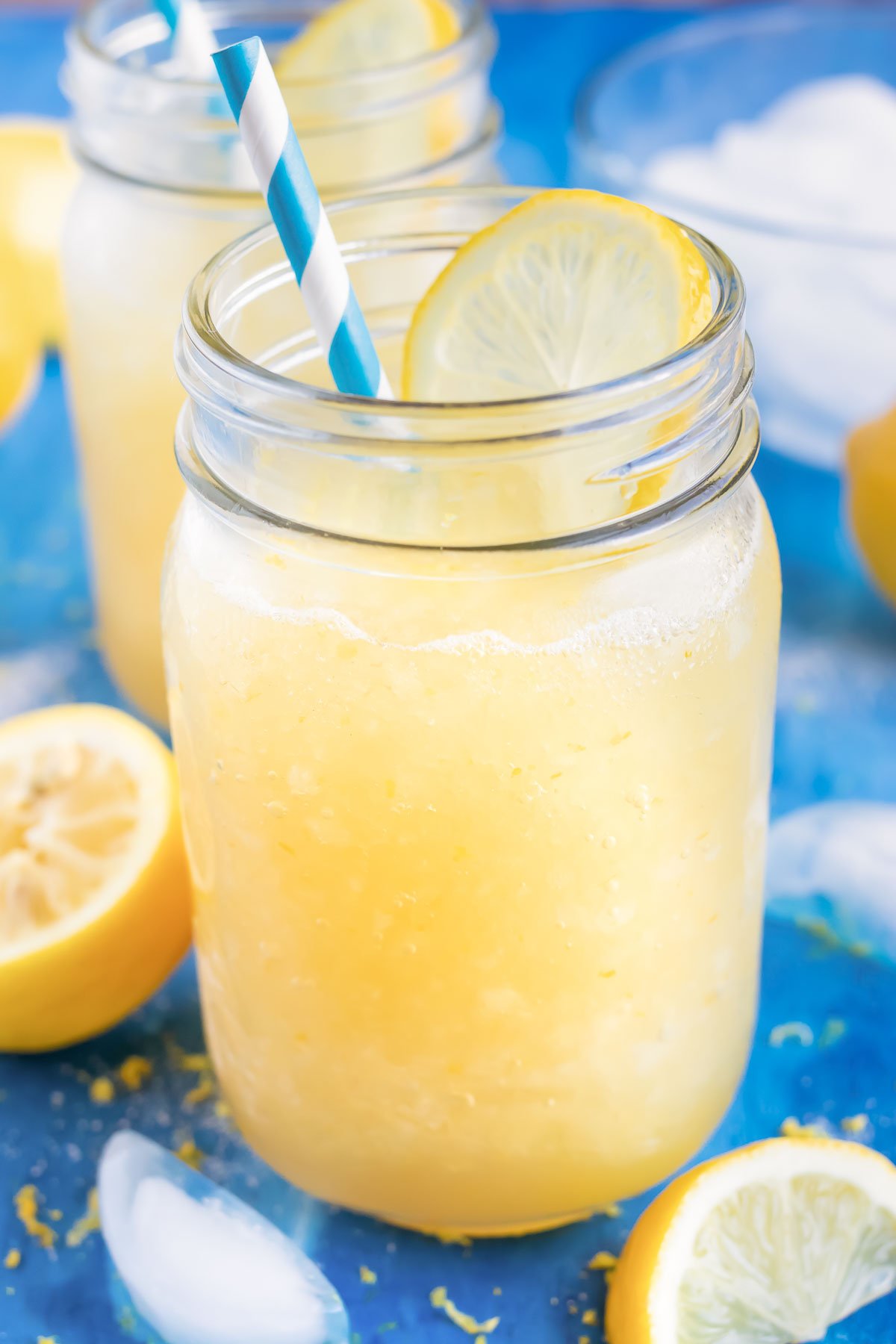 Homemade frozen lemonade in a glass mason jar with a blue straw next to a lemon wedge.