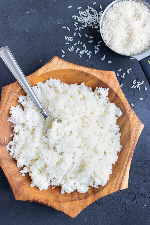 Cooked white rice in a wooden bowl with a spoon in it.