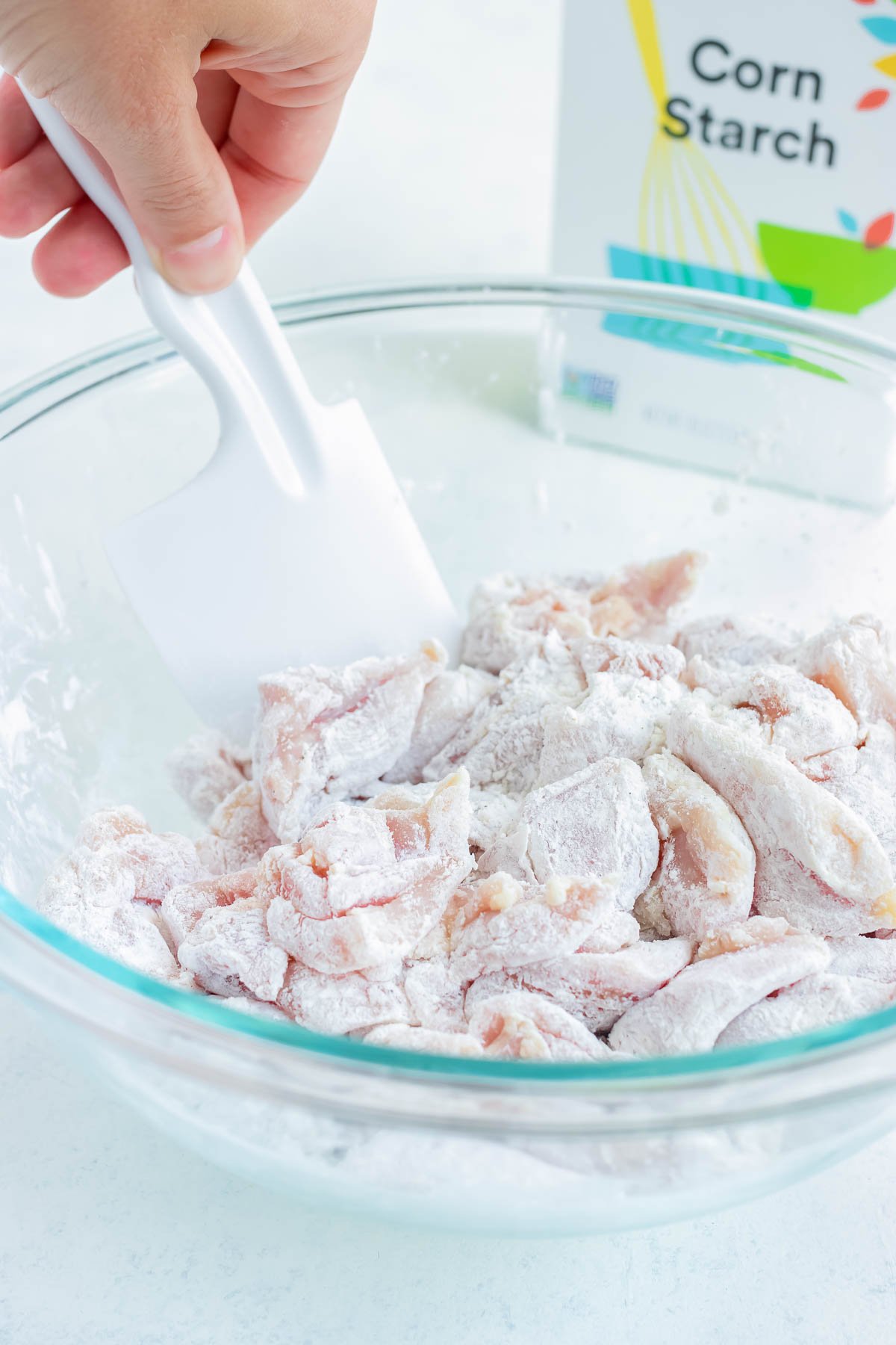 Raw chicken cubes are being coated in a mix of flour and corn starch in a bowl.