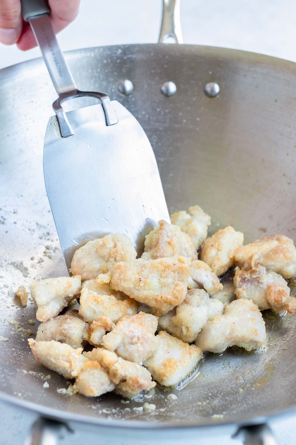 The chicken is lightly fried in a skillet on the stove.