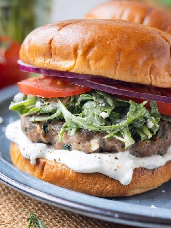 Greek turkey burgers with spinach and feta cheese are served with tzatziki sauce on a plate.