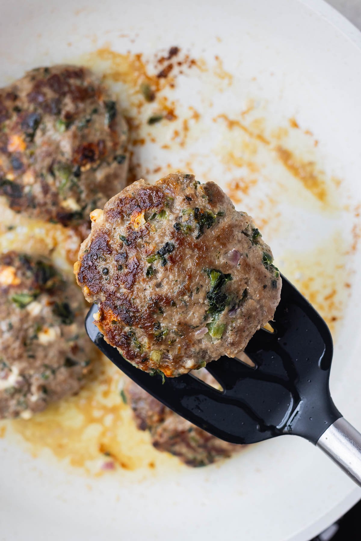 A spatula picks up a cooked burger patty.