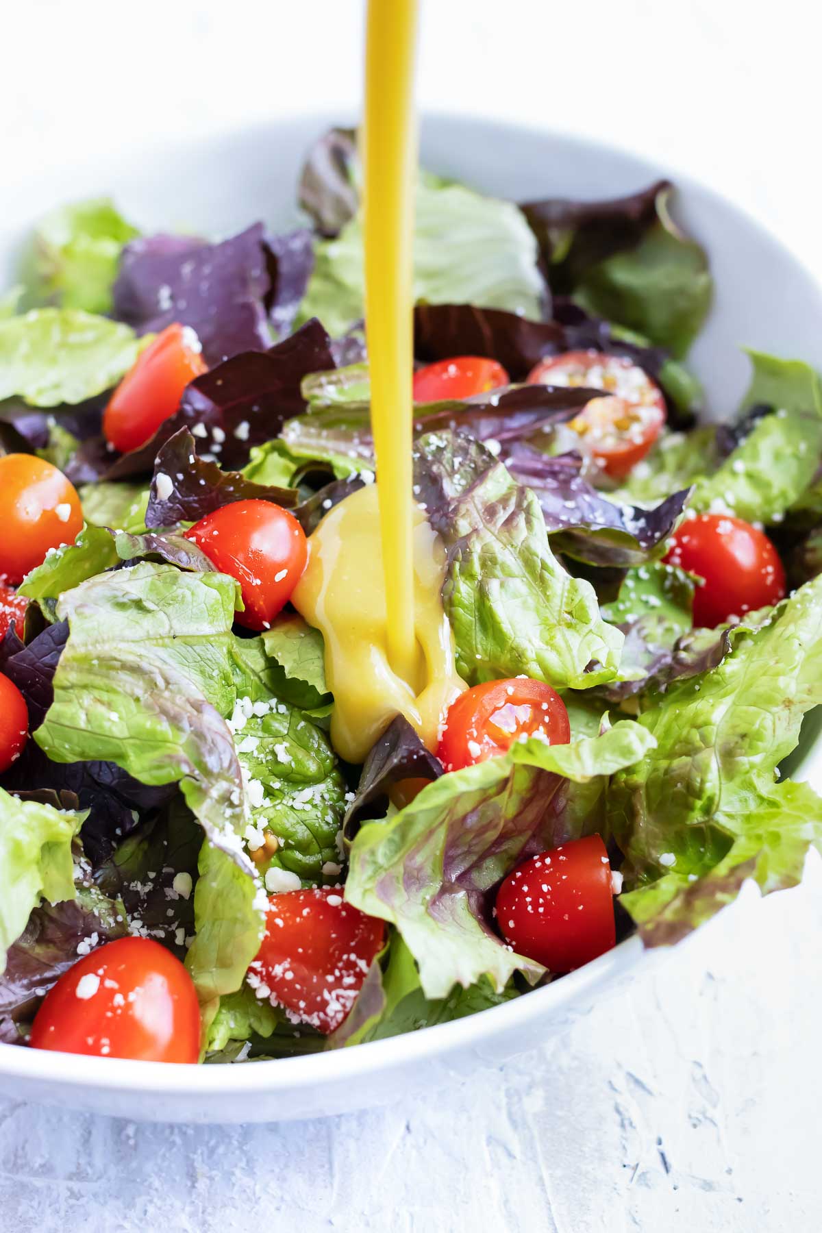 Honey mustard dressing being poured onto a salad with mixed greens and tomatoes.