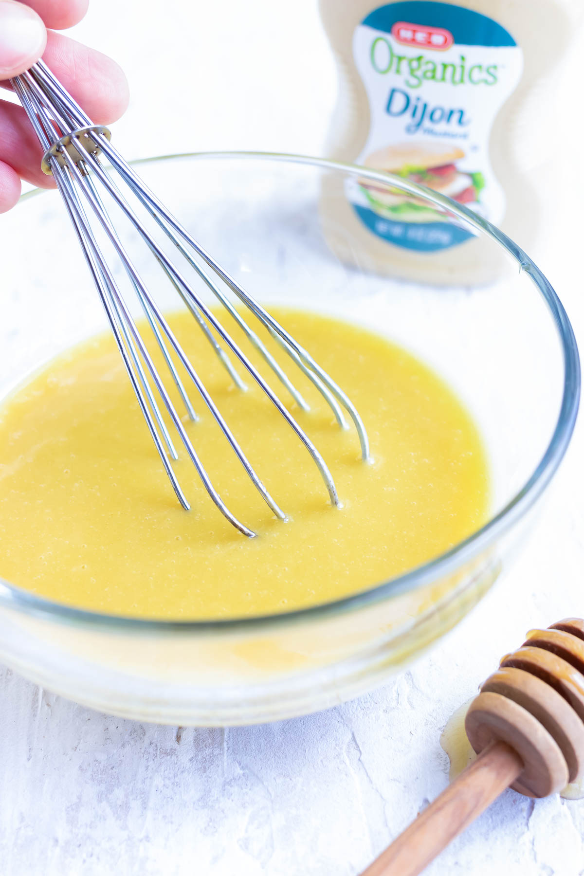 A clear bowl with honey mustard salad dressing being whisked together.