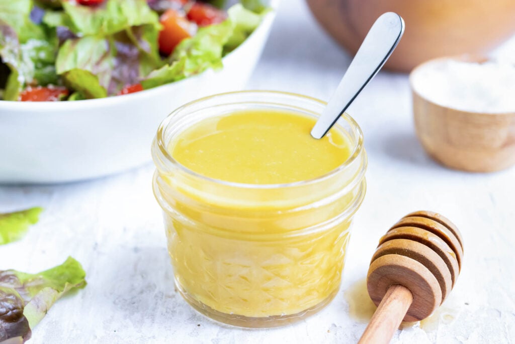 Creamy homemade honey mustard vinaigrette in a small glass jar with a spoon.