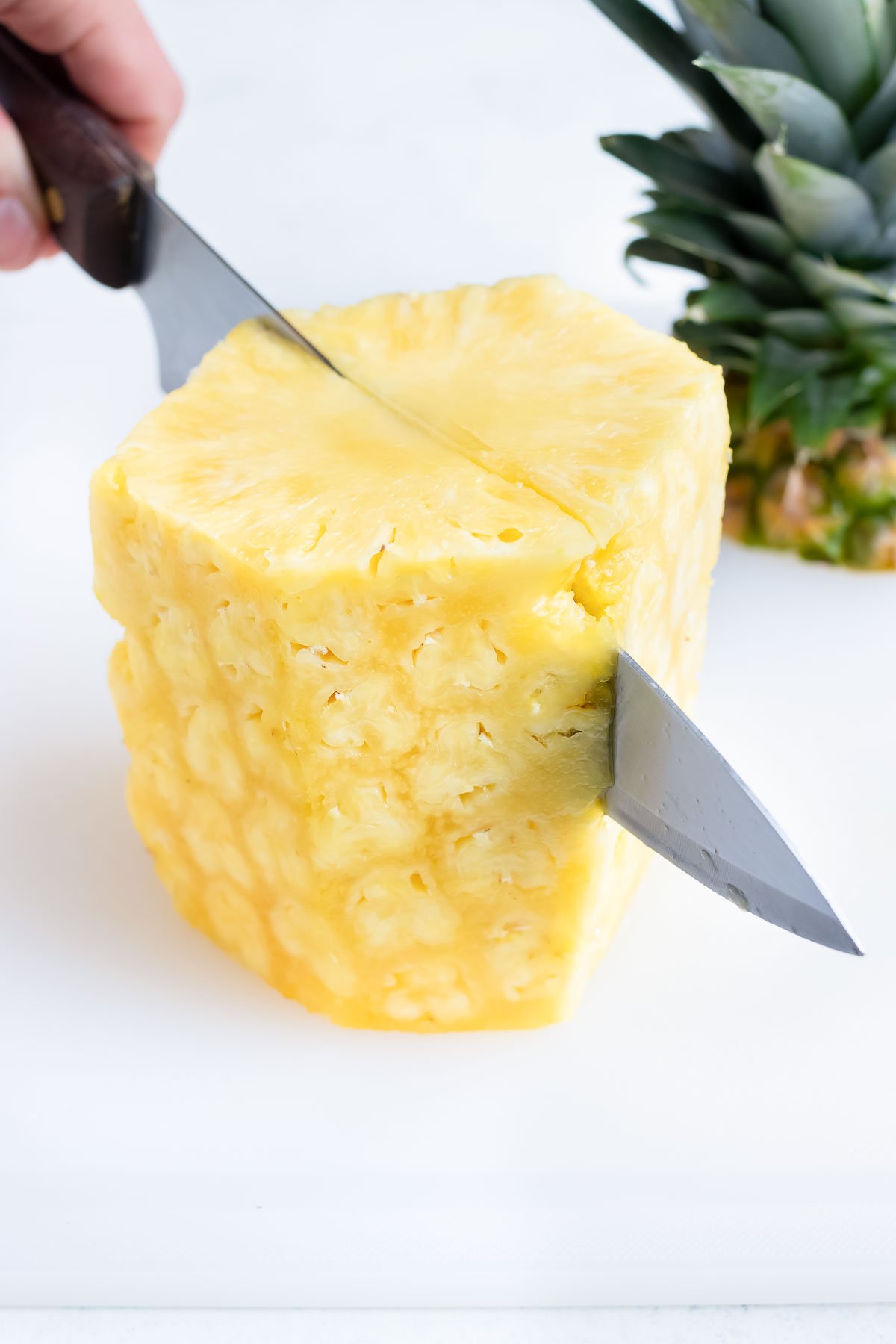 Cutting a trimmed, whole pineapple down the middle from the top.