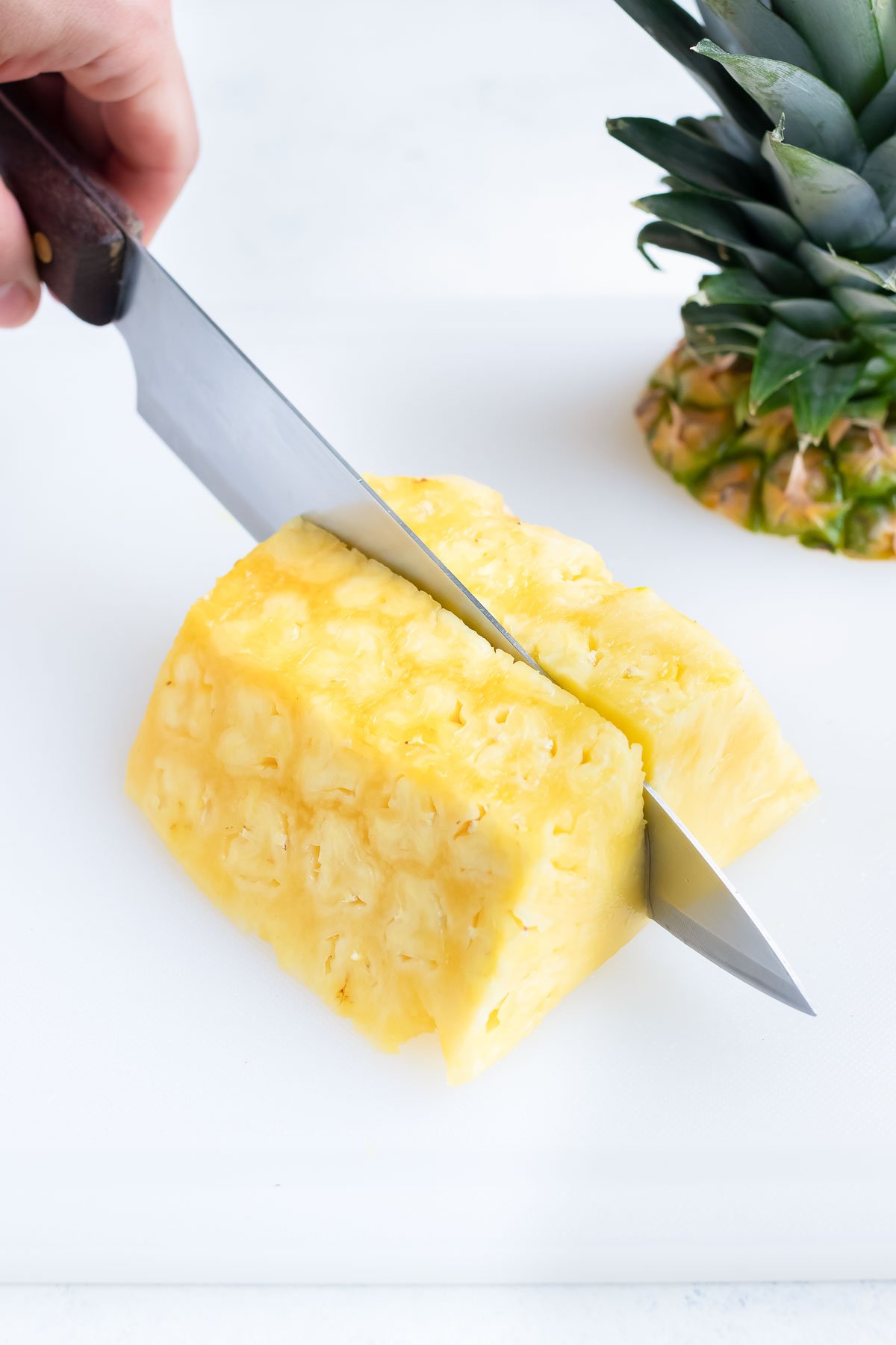 Cutting a trimmed, halved pineapple down the middle.