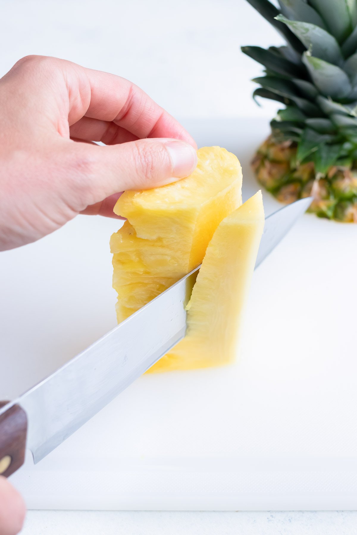 Cutting pineapple flesh around the pineapple core with a sharp knife.