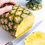 A knife is used to cut off the bottom end of a pineapple.