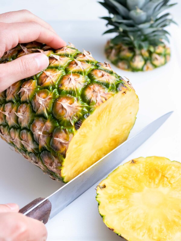 A knife is used to cut off the bottom end of a pineapple.