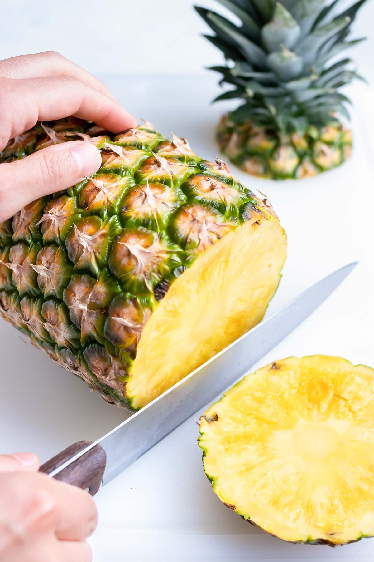 A knife cutting off the bottom end of a pineapple.