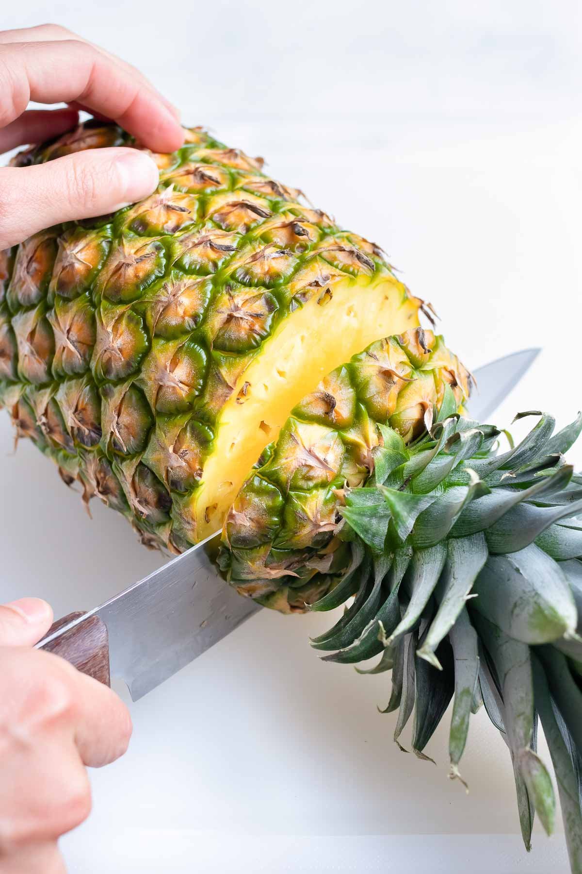 Cutting the top of a pineapple off.