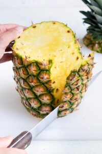 The skin is removed from the whole pineapple with a knife.