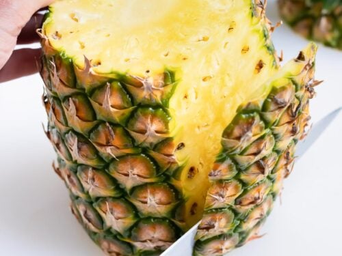 The skin is removed from the whole pineapple with a knife.