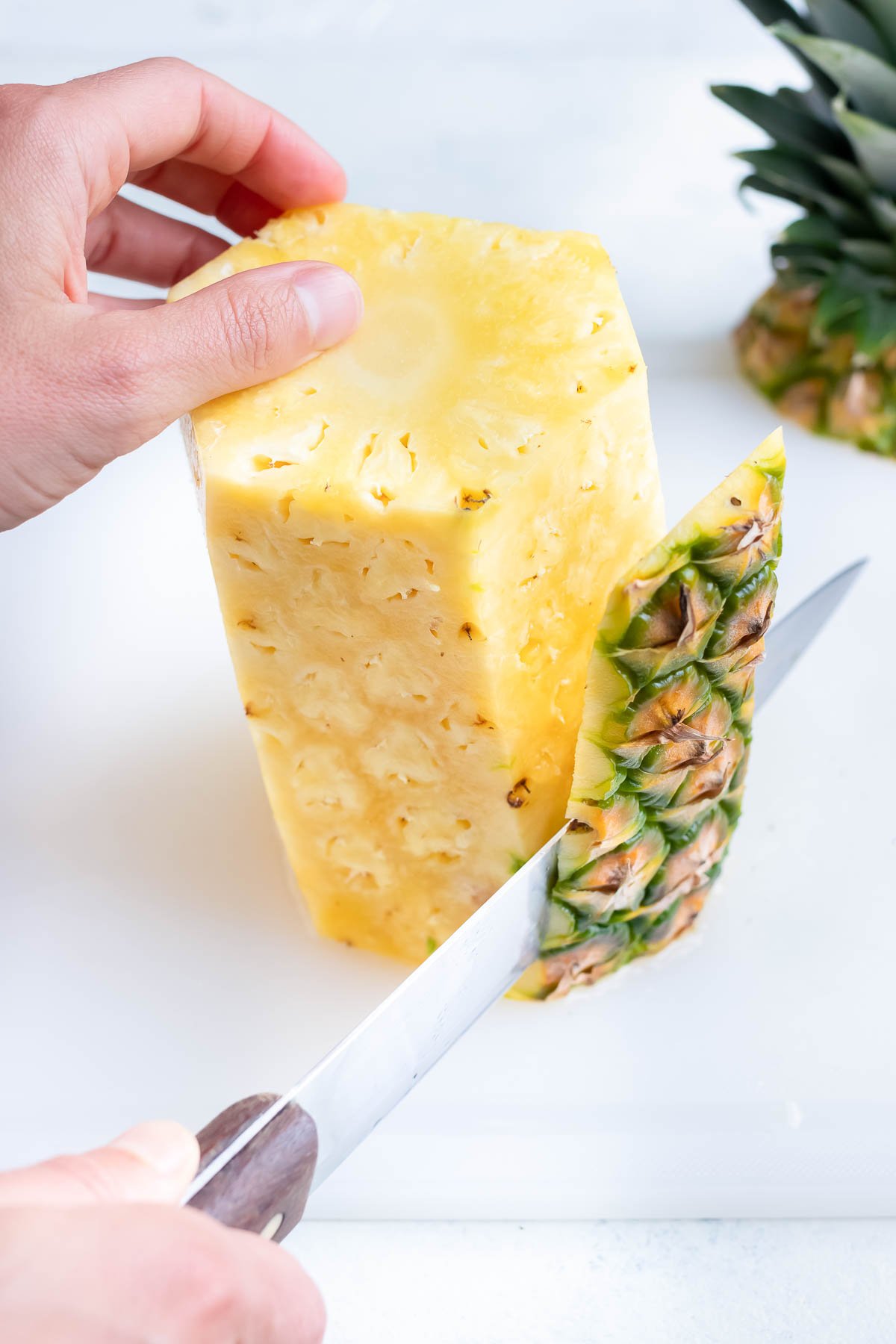 The whole pineapple skin is removed with a knife.