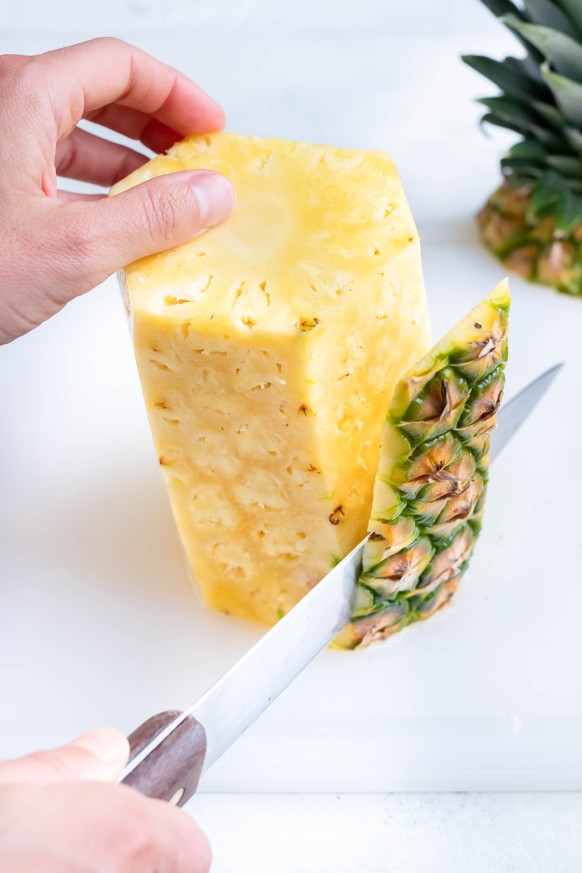 Cutting the side of a pineapple with a sharp knife.