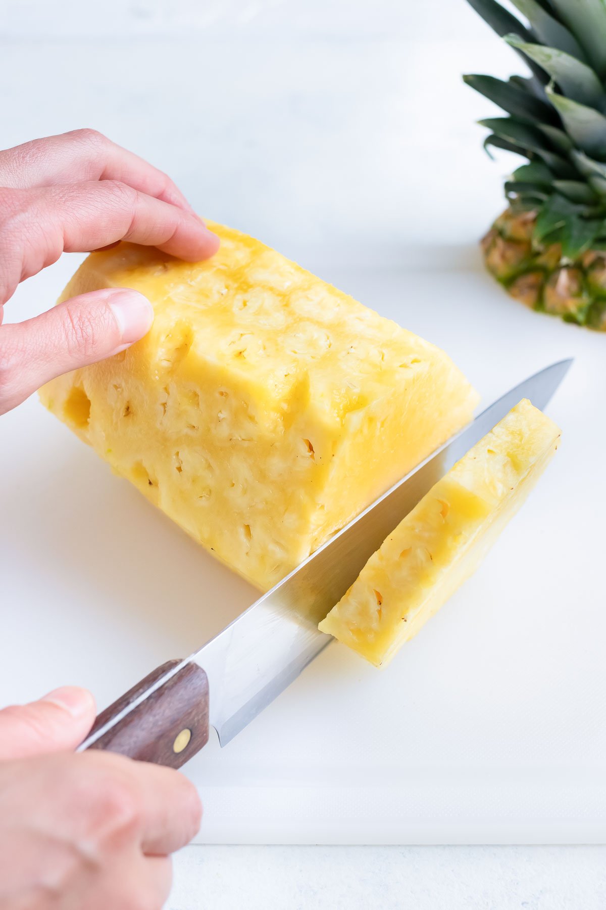 Cutting a trimmed, whole pineapple in slices.